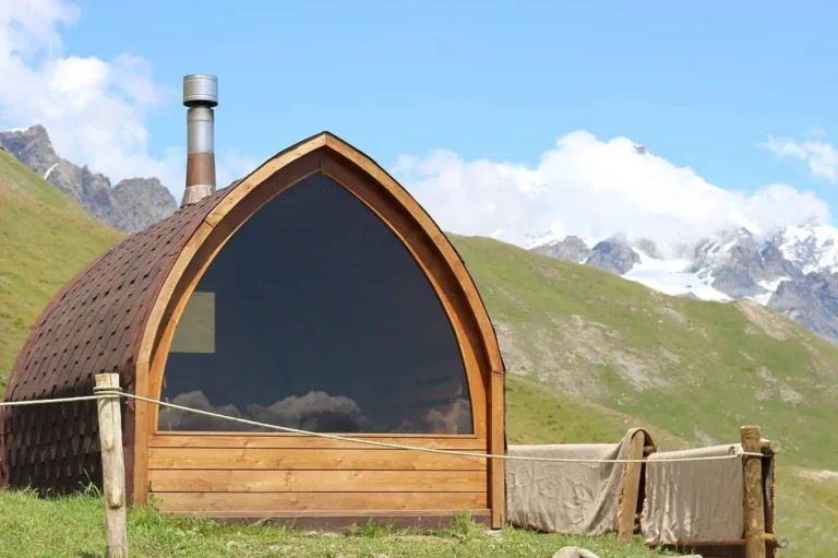 A rustic wooden outdoor sauna cabin with a window, nestled in a stunning mountain landscape—perfect inspiration for learning how to build an outdoor sauna.