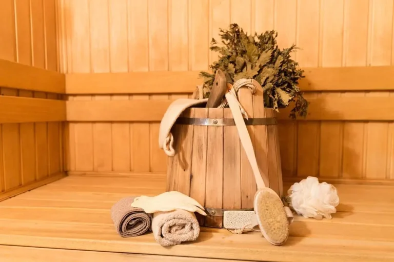 Exploring if sauna helps sore throat with natural remedies: A wooden bucket filled with herbs, towel, and brush in a cozy spa-like setting.