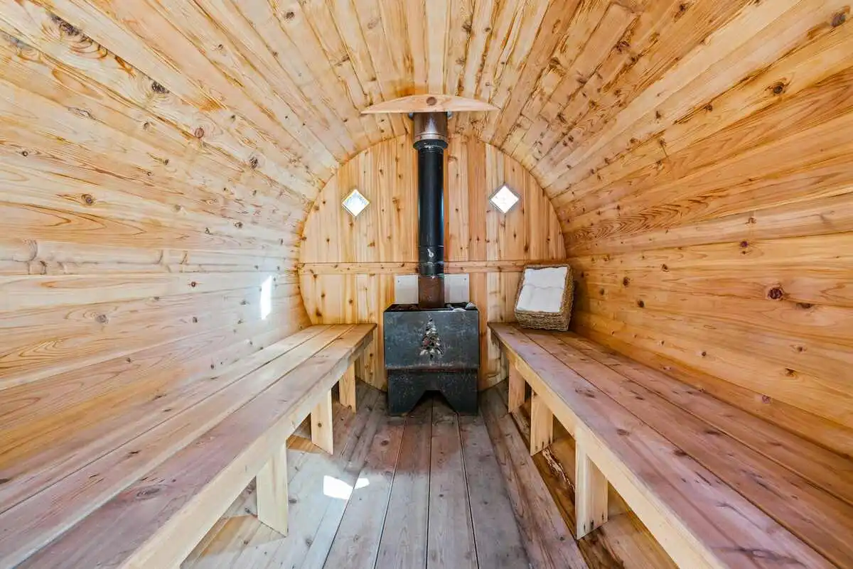 A rustic wood-fired stove and wooden benches inside a cozy cabin, illustrating key elements for how to build an outdoor wood-fired sauna.