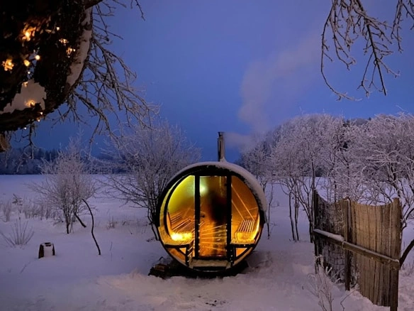 A small wooden Finnish outdoor sauna covered in snow, showcasing a serene winter scene—inspiration for how to build a Finnish outdoor sauna.